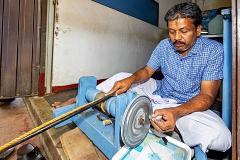 A concentrated man sits at a grinding machine and works on an object, The gemstone cutters in the