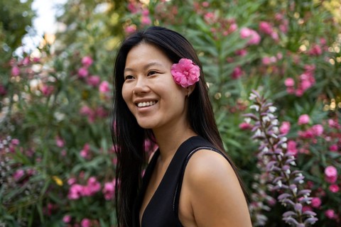 A Chinese woman with a pink flower in her hair smiles joyfully during a sunny summer day in the