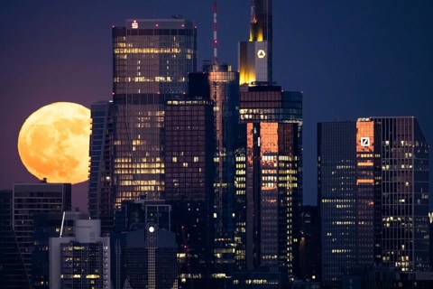 The full moon passes behind the Frankfurt banking skyline, Frankfurt am Main, Hesse, Germany