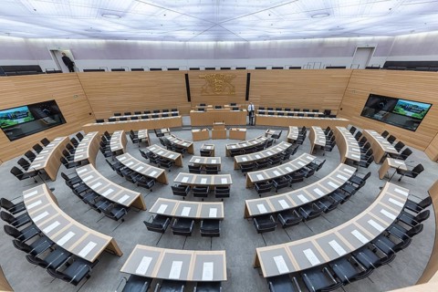 Plenary hall deserted with the seats of deputies and the government bank. Behind it is the coat of