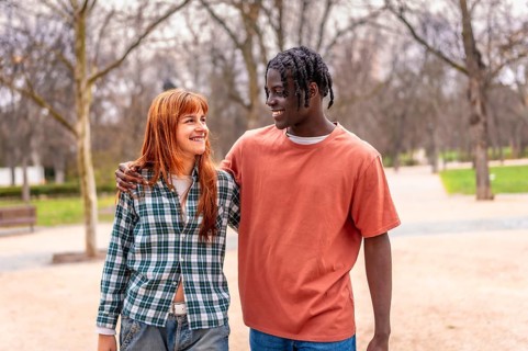 Young multiracial couple walking together in a park, chatting and smiling while enjoying each