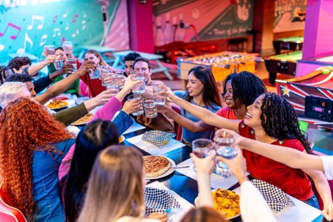 Cheerful young multiethnic friends raising glasses for a toast, enjoying food and drinks at a
