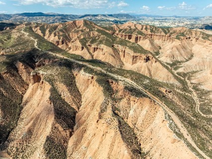 Winding gravel road on a plateau, surrounded by colorful canyons and gorges, aerial view, Gorafe