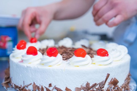 Person decorating cake with cherries on cream, surrounded by chocolate, cake baking, Haselstaller