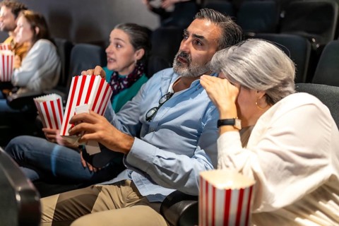 Group of friends and family enjoying a movie at the cinema, eating popcorn and showing a wide range