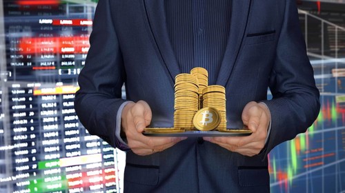 Man in suit holding Bitcoin coins in front of blurred financial data and graphics in the