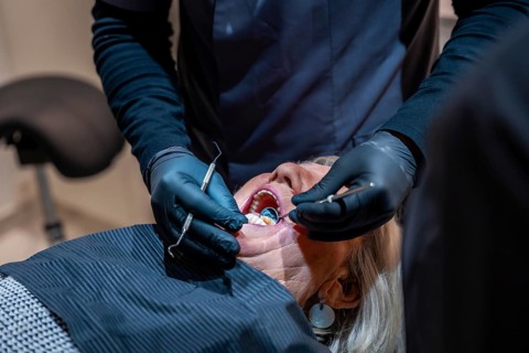 Dentist wearing black gloves examining teeth of a senior woman lying in dentist chair during a
