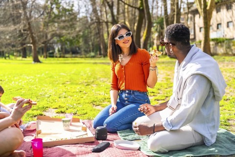 Young people enjoying a sunny day picnic in a city park, sharing delicious pizza and laughter while