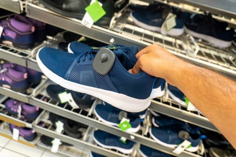 A person is holding a blue shoe with a tag on it. The shoe is on display in a store