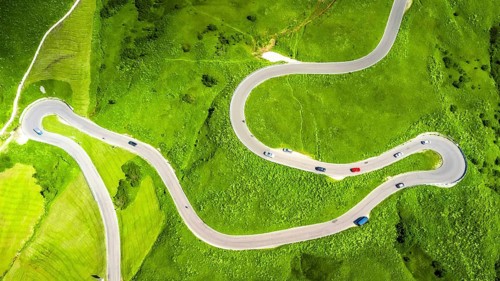 Winding road seen from above with cars driving on a green meadow in the italian dolomites mountains