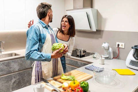 Happy couple cooking together in a bright, modern kitchen, sharing laughter and joy while preparing