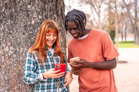 Two happy multi ethnic students sharing funny content on their mobile phones while leaning on a