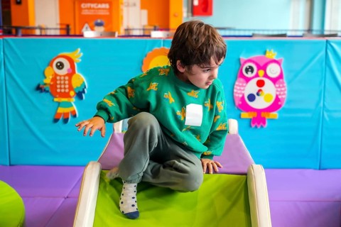 Young boy having fun crawling on a soft slide in a colorful indoor playground, enjoying his