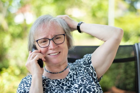Outdoor shot, elderly woman, glasses, dressed in summer clothes, sitting in the garden, talking on