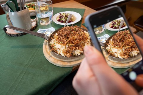 Guest taking photos of his food with his mobile phone, cheese spaetzle in a pan, Bavaria, Germany