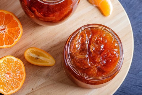 Tangerine and kumquat jam in a glass jar with fresh fruits on a black wooden table. Homemade, close