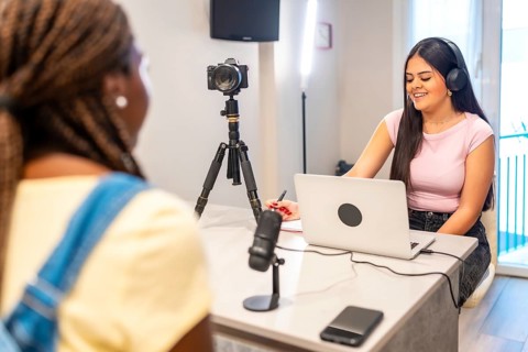 Two teenage girls creating digital content with laptop, camera, microphone, and headphones,