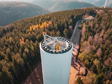 Bird's eye view of a wind turbine under construction, with a view of an extensive forest landscape,