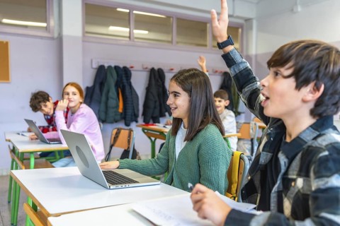 Elementary school students raising hands and using laptops in an interactive classroom, engaging in
