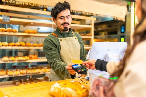Rear view of a latin woman paying using credit card in an artisan modern bakery