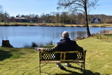 Man sitting with a coffee cup on a bench by a lake, Schleswig-Holstein, Germany