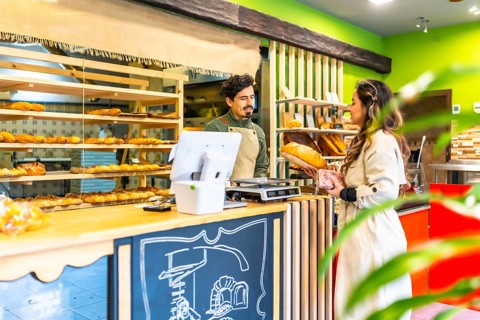 Woman talking to salesman next to the counter while buying bread in artisan bakery