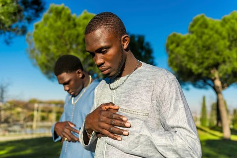 Two senegalese men wearing traditional grand boubou are praying in a park during the holy month of