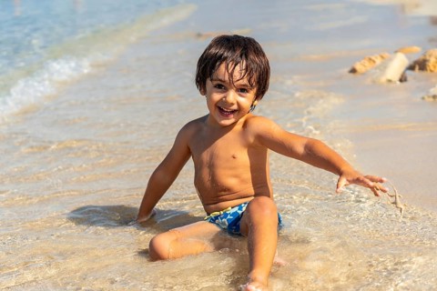Smiling boy enjoying summer vacation, playing in the waves on the beautiful sandy beach of estanys