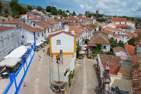 Medieval village with white houses and red roofs, lively with tourists, inviting and sunny, view