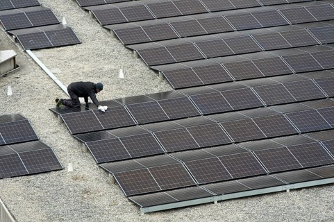 Technician cleans solar panels on the flat roof of the Varembé indoor swimming pool, Piscine de