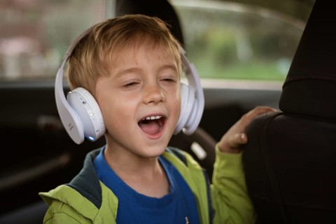 Six years old boy with headphones singing in the car