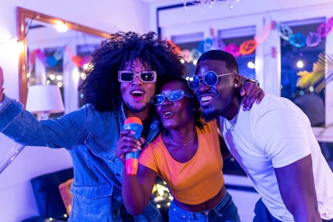 Three multi-ethnic friends enjoying karaoke singing with toy mic at night home party