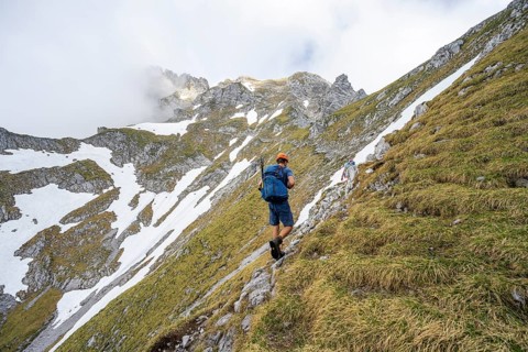 Mountaineer with helmet on a narrow hiking trail, ascent to the Ackerlspitze, clouds moving around