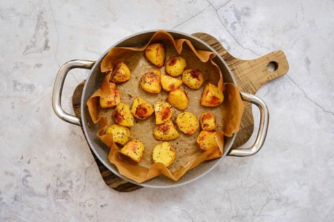 Golden brown roasted potatoes are beautifully arranged in a serving platter lined with parchment