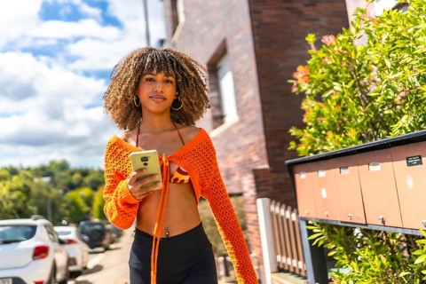 Brunette beauty woman using phone in the street walking along a residential area