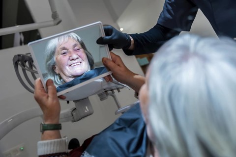 Dentist showing a mirror to a senior patient, revealing her perfect smile after a successful dental