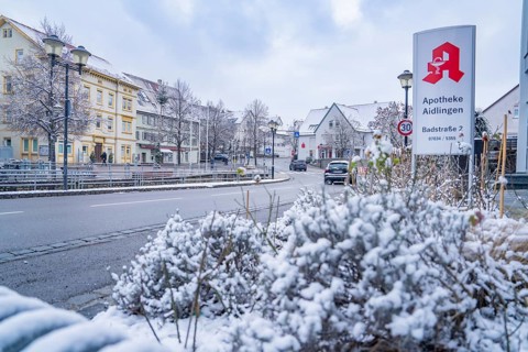 Snow-covered town street with pharmacy sign and surrounding buildings, Aidlingen, Böblingen