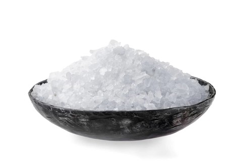 A large pile of sea salt is beautifully presented in a decorative bowl set against a simple neutral