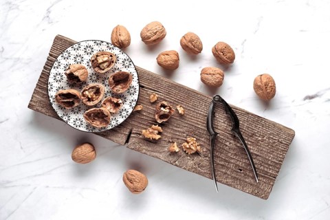 A rustic setup features whole and cracked walnuts on a patterned plate, with a nutcracker beside