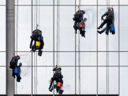 Employees of a cleaning company work vertically hanging on a rope while cleaning a glass façade on