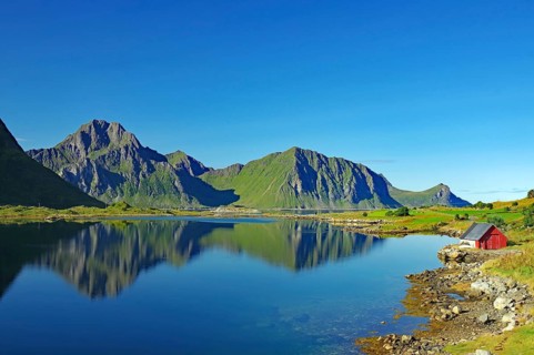 A small lake surrounded by mountains and a red house reflects the landscape, Leknes, Vestvågøya,