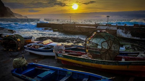 Harbour with colorful fishing boats and setting sun over the stormy sea, romantic harbor scene,