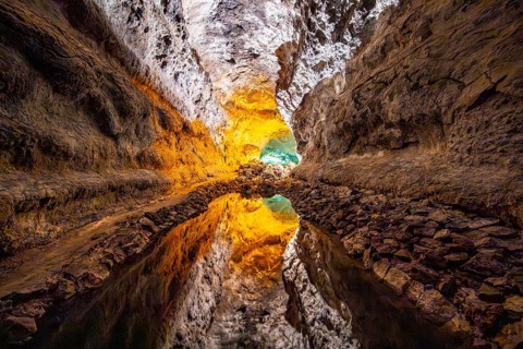 Lava tunnel, illuminated lava cave with perfect reflection in an underground lake, Cueva de los
