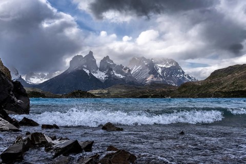 Cuernos del Paine with snow-capped peaks under dramatic cloud cover, storm-swept Lake Pehoé with