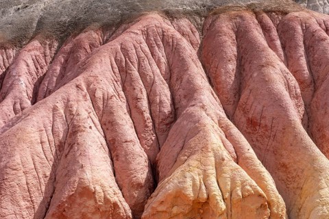 Eroded rock formation with pink, reddish and yellowish layers of color, washed out channels and