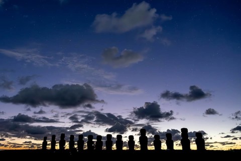 Silhouettes of the fifteen Moai statues of Ahu Tongariki against a starry sky and clouds at dawn,