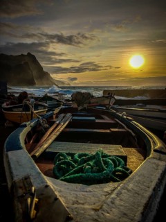 Colorful fishing boats on the shore with ropes and setting sun over the sea, dramatic coastal