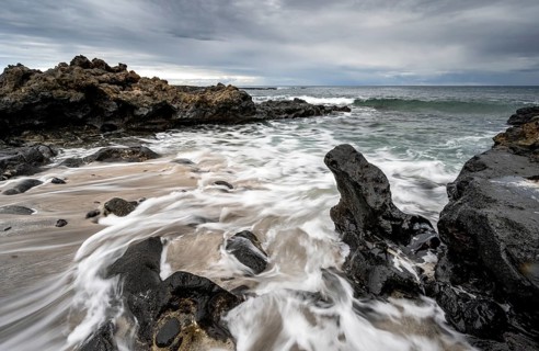 Waves blaze on the beach, rocky coast with volcanic stones, long exposure, Playa de la Pequeña,