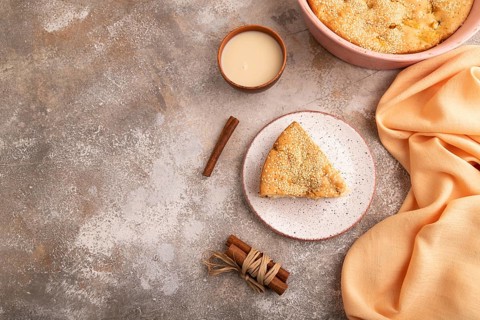 Apple Charlotte cake on brown concrete background and orange linen textile, cup of milk, top view,