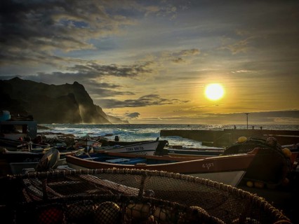 Several boats in a harbor with setting sun over the sea, fish net, golden waves frame the scene,